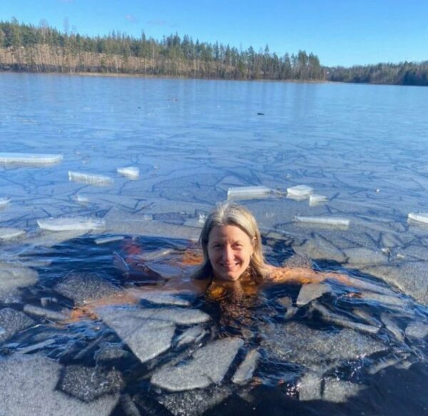 Leende kvinna som tittar upp med huvudet ur en i övrigt frusen sjö